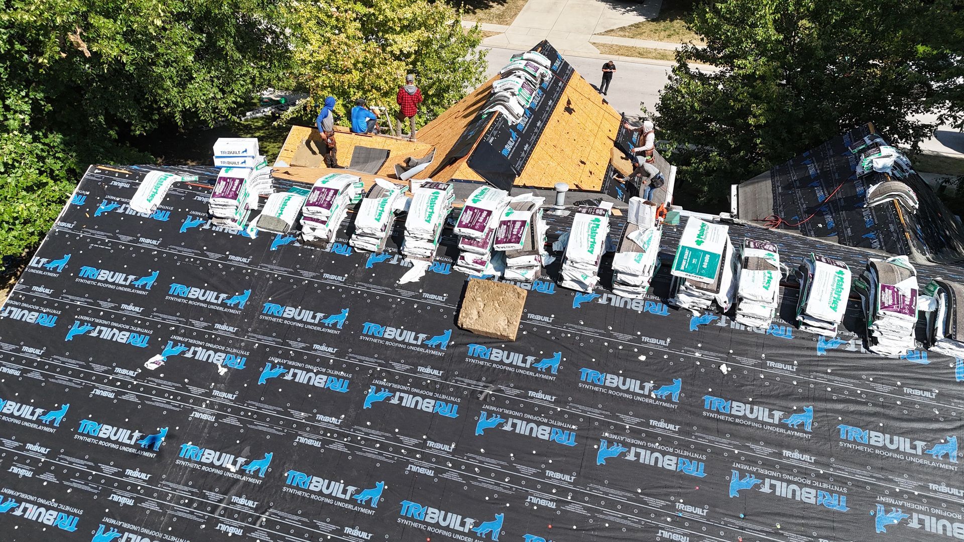 Workers installing shingles on a residential roof covered with black underlayment.