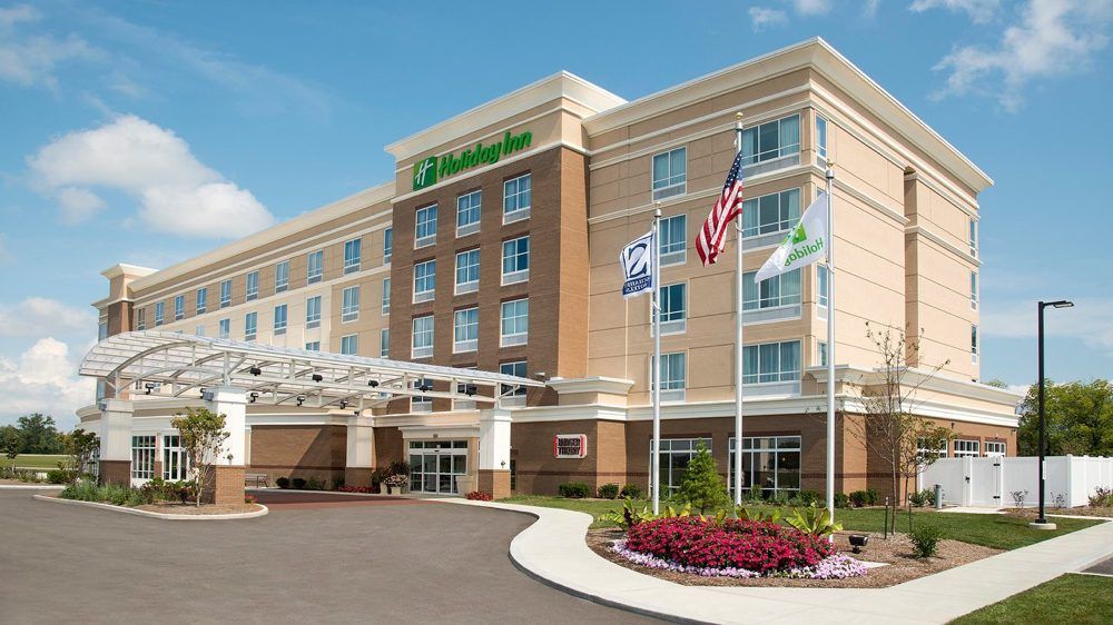 Exterior of a modern hotel with a covered entrance, American flag, and landscaped driveway