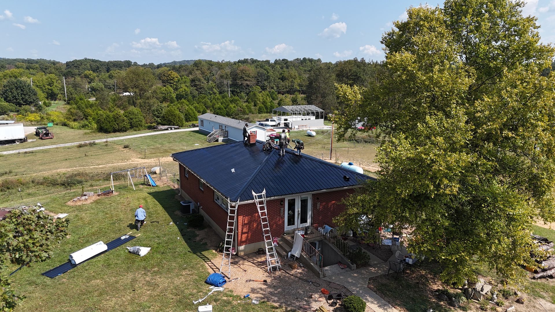 An aerial view shows roofers installing a dark metal roof on a red house in Indianapolis